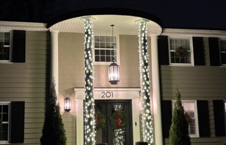 Warm-white lights wrapped around colonial entry columns with holiday wreaths at a Northeast Wisconsin home, by Lighting Squad