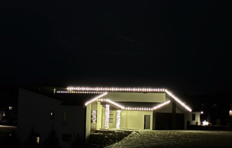 Warm-white roofline Christmas lights outlining the eaves and porch columns of a modern home, by Lighting Squad