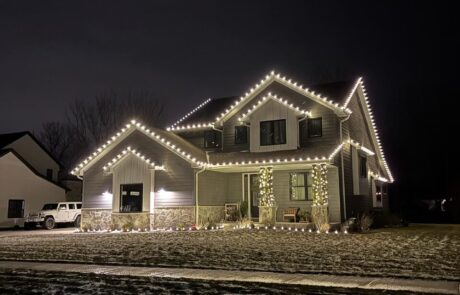 Warm-white roofline Christmas lights on a craftsman-style home with lit porch columns, by Lighting Squad