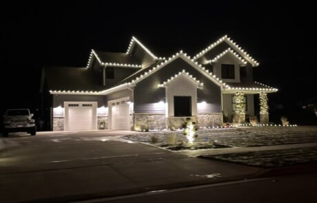 Warm-white roofline holiday lights outlining a large two-story home and three-car garage, by Lighting Squad