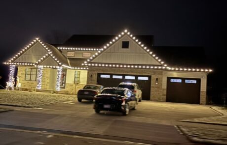 Warm-white roofline Christmas lights on a home with lit entry columns at dusk, installed by Lighting Squad